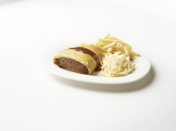White plate of knish with a side of french fries and coleslaw on a white background