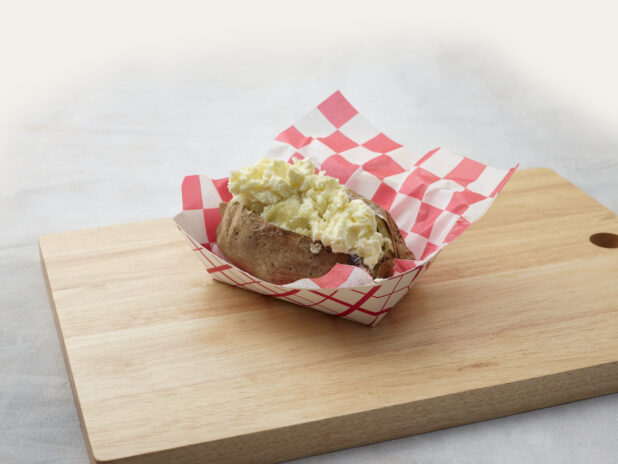 Baked potato stuffed with egg salad in a basket on a wooden board