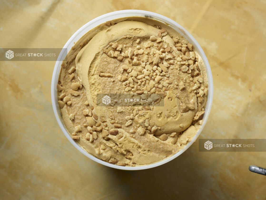 Overhead view of a large tub of caramel swirl ice cream with cookie crumble on a yellow background