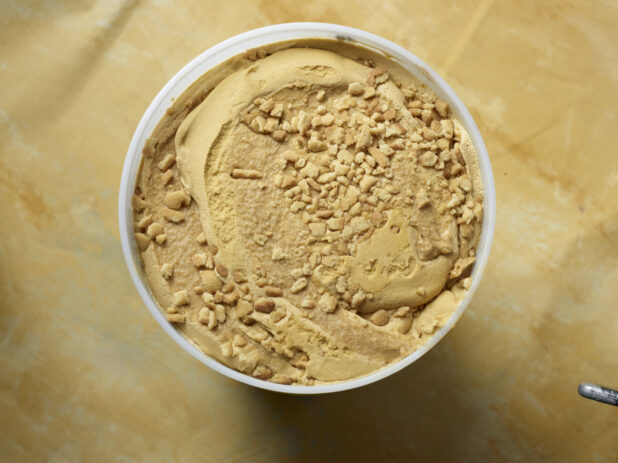 Overhead view of a large tub of caramel swirl ice cream with cookie crumble on a yellow background