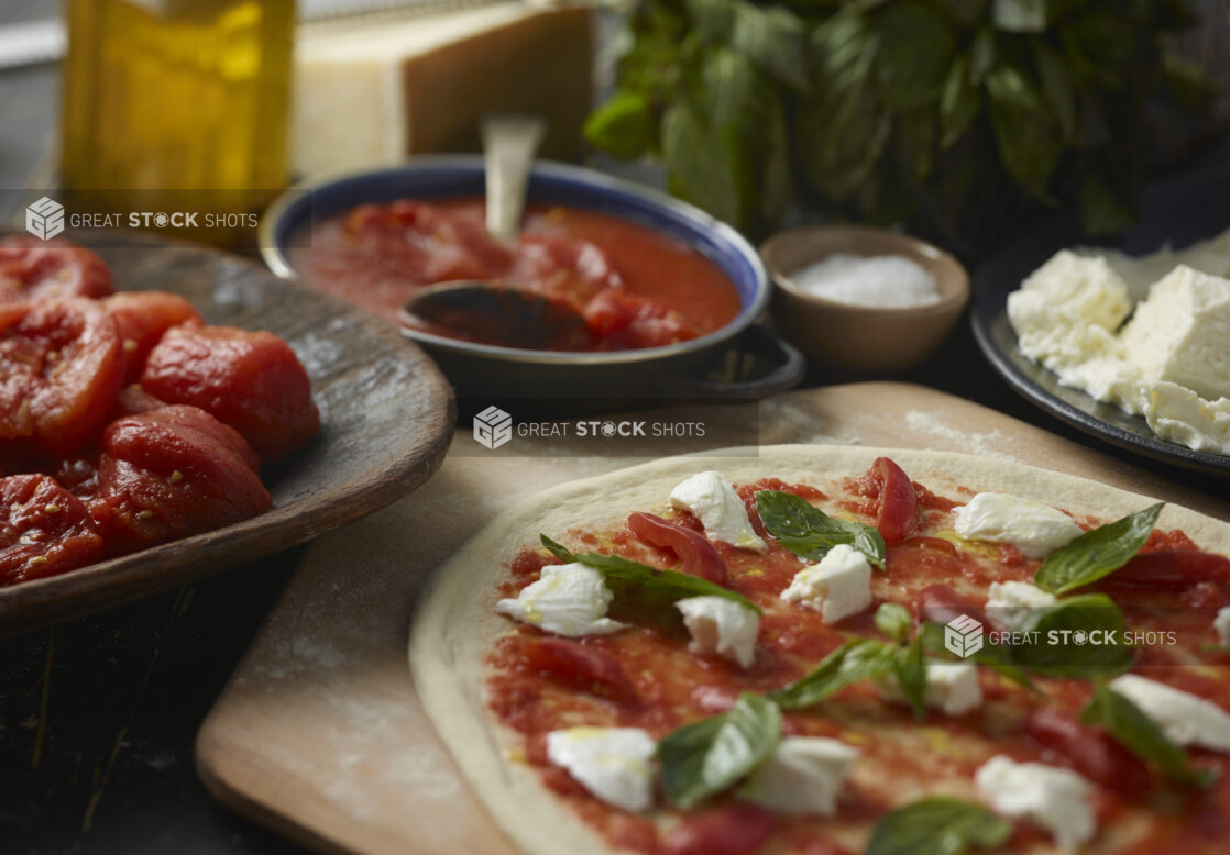 Uncooked Margherita pizza on peel with ingredients in the background