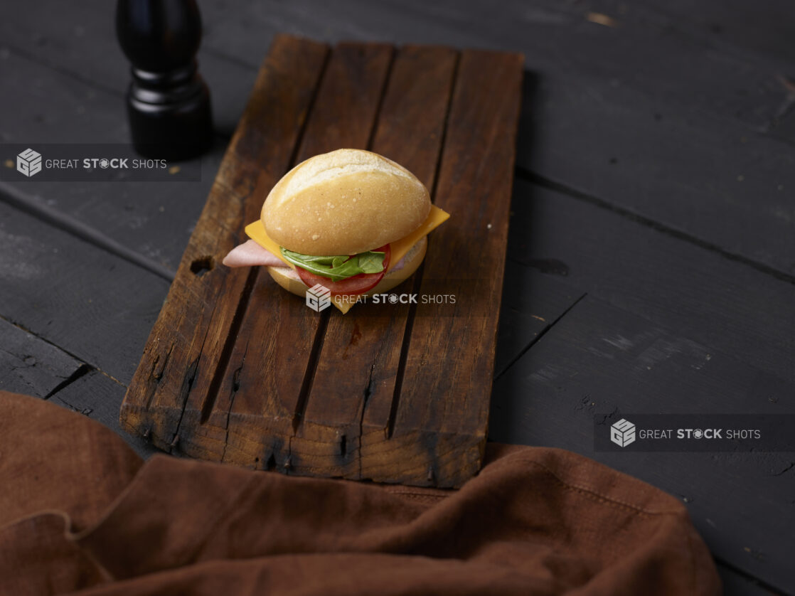 Ham and cheese sandwich on a white bun on a wooden board with a napkin