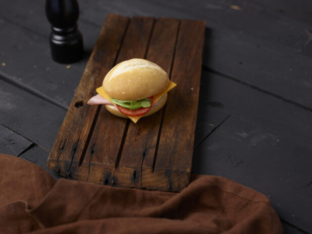Ham and cheese sandwich on a white bun on a wooden board with a napkin
