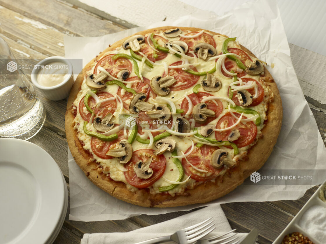 Whole vegetarian pizza on parchment paper with a side creamy dip on top of a wooden background