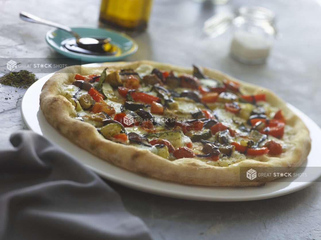 Whole vegetarian pizza with a balsamic drizzle on a large white plate on a slate background, close-up