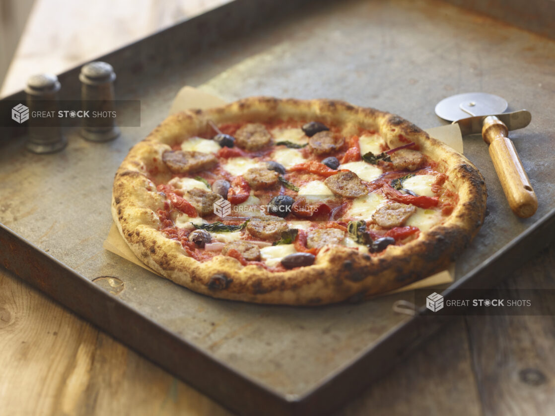 Whole four-topping pizza on a metal board with a pizza cutter and salt and pepper shakers