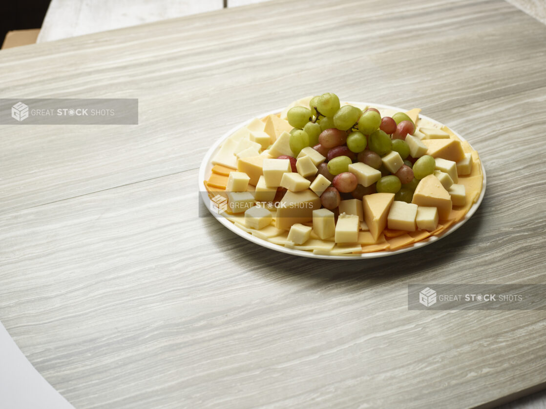 Large assorted cheese and grape platter on a white plate on a wooden background