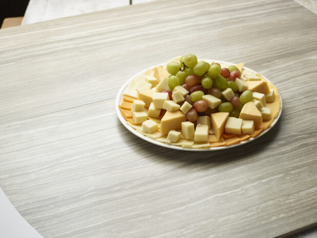 Large assorted cheese and grape platter on a white plate on a wooden background