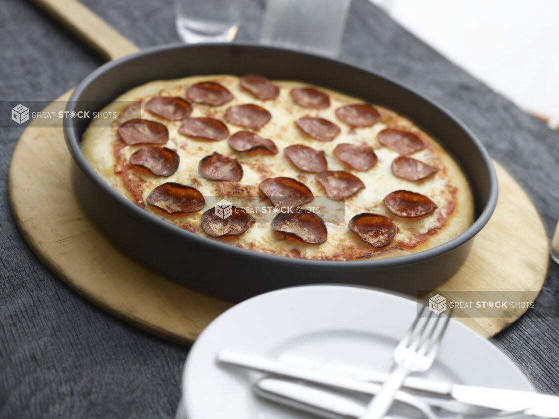 Full deep dish pepperoni pizza on a wooden peel on a black wooden background