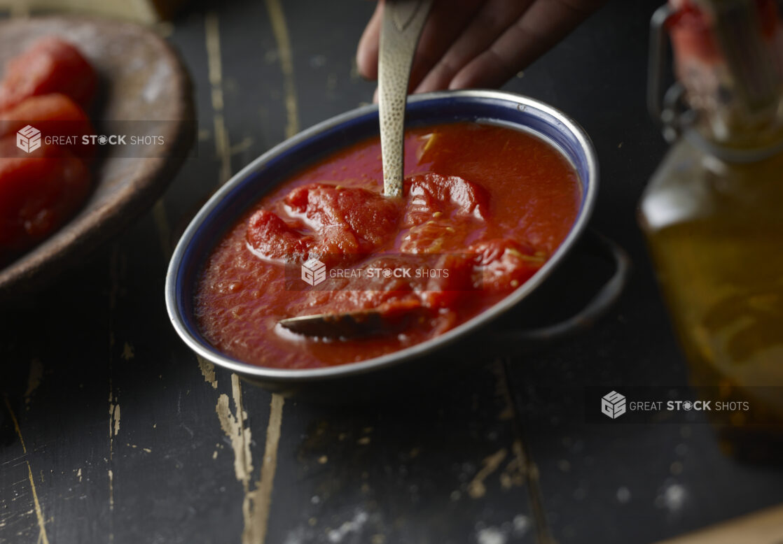 Bowl stewed tomatoes on a black distressed wooden background, close-up