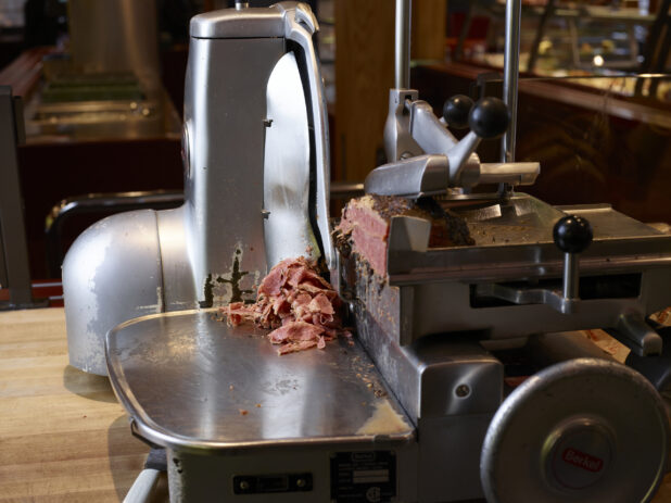 Side view of commercial grade meat slicer, shaving pastrami in a restaurant