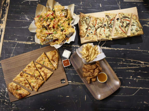Various appetizers including nachos, flatbreads, chicken tenders and fries, overhead on a dark distressed background