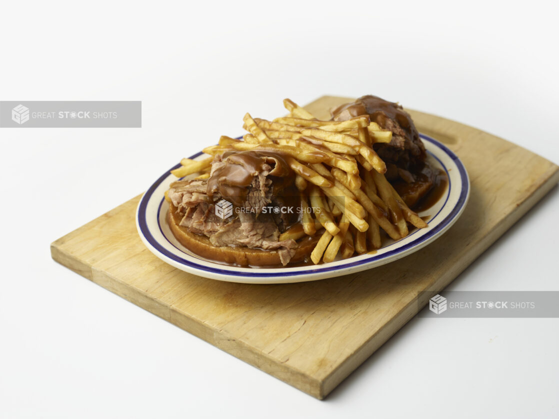 Hot open-faced roast beef sandwich on rye with gravy and french fries on a wooden board on a white background