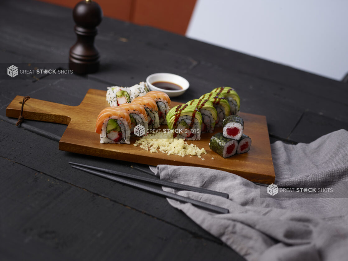 Various sushi rolls on a wooden cutting board with chopsticks