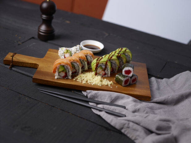 Various sushi rolls on a wooden cutting board with chopsticks