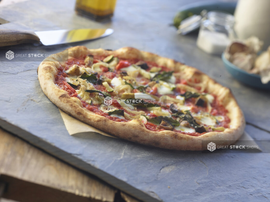 An artichoke and eggplant individual pizza on parchment on a grey slate tabletop