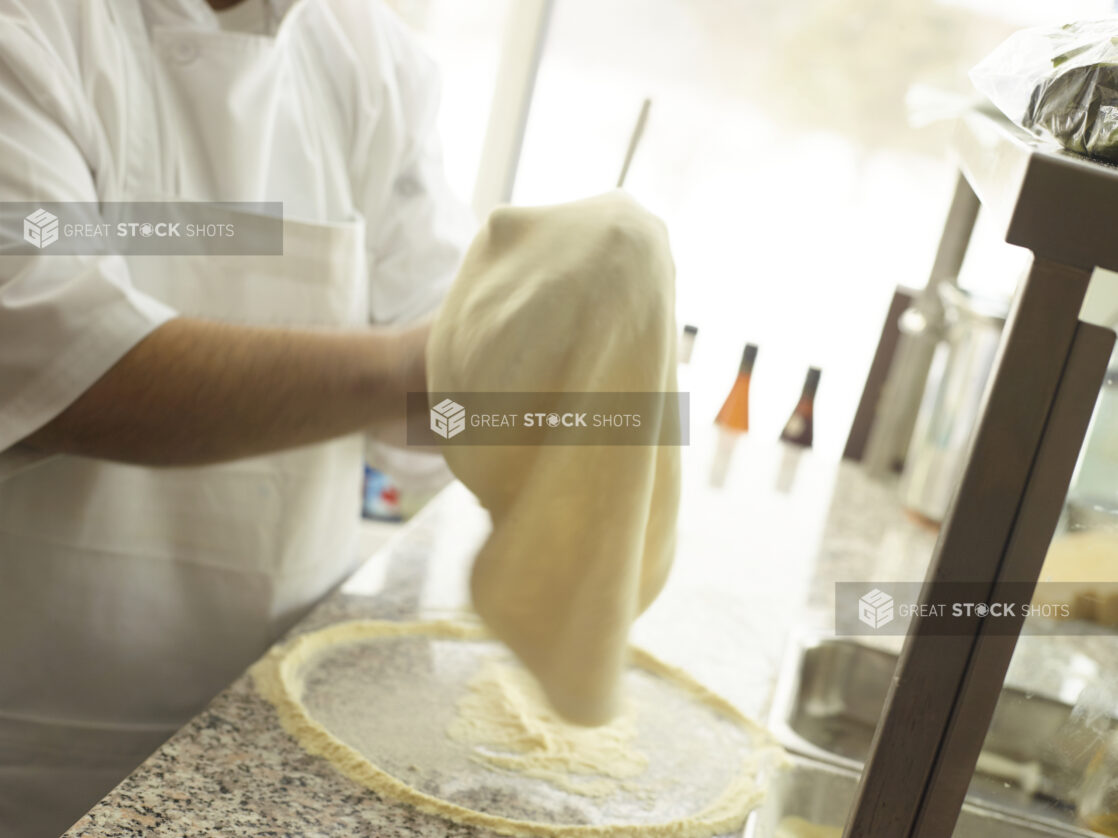 Pizza chef stretching a pizza dough over a cornmeal-coated marble work surface