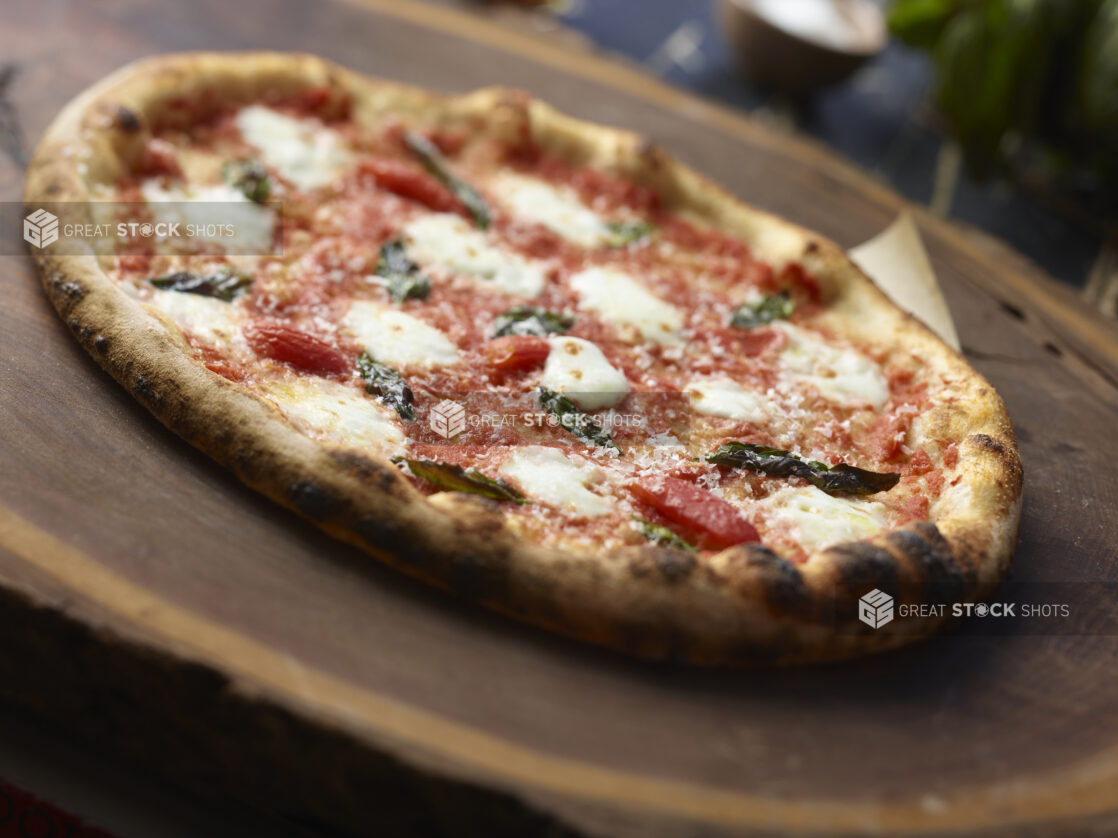 Whole margherita pizza with basil topped with fresh parmesan cheese on a dark wooden board, close-up