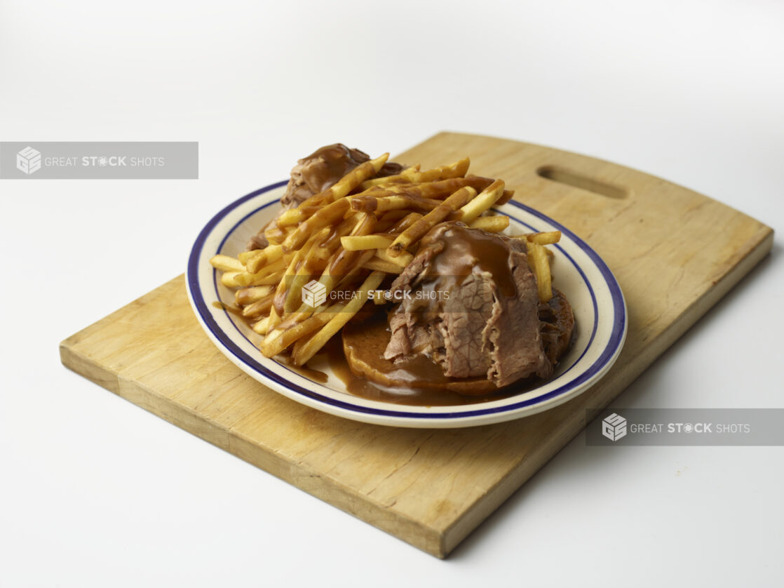 Hot open-faced roast beef sandwich on rye with gravy and french fries on a wooden board on a white background