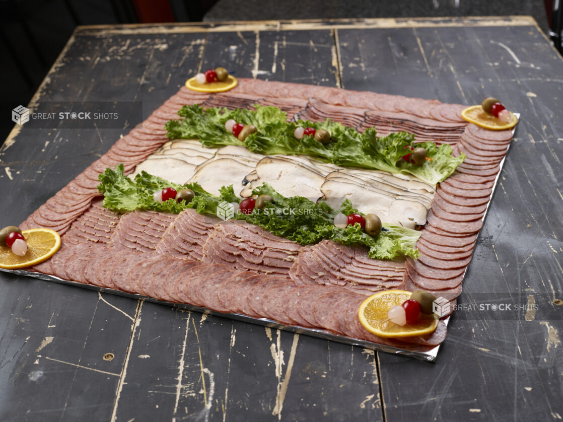 Platter of mixed deli meats with garnish on a distressed black wooden background