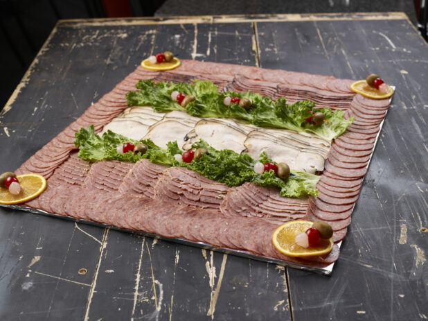 Platter of mixed deli meats with garnish on a distressed black wooden background