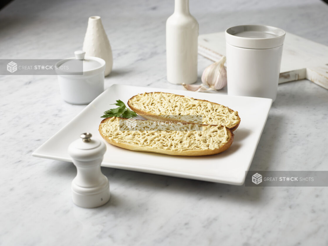 Two halves of garlic bread with dairy-free cheese on a white plate on a white marble background