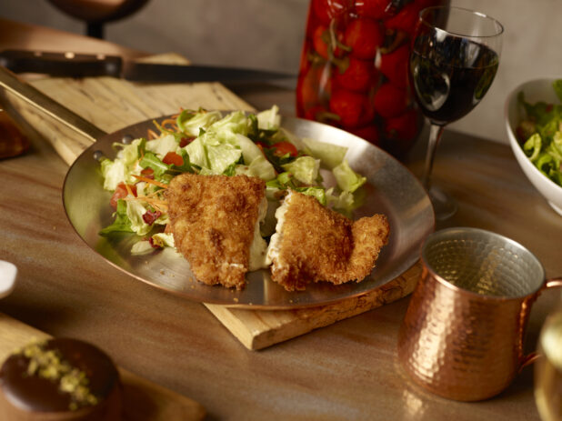 Crispy chicken cordon bleu with side garden salad on a metal frying pan