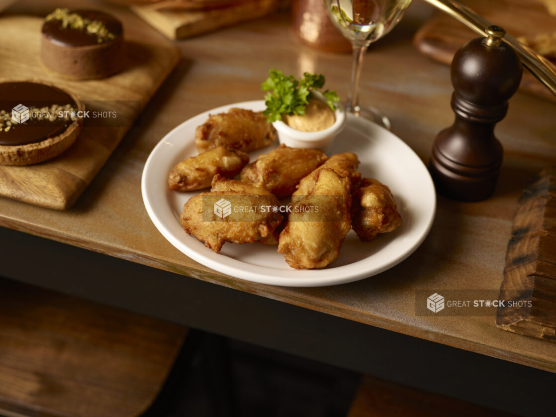 Battered chicken wings on a white plate with dip on a wooden table