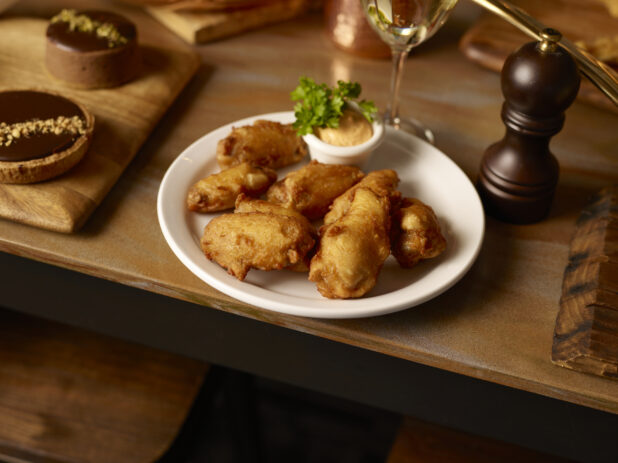 Battered chicken wings on a white plate with dip on a wooden table