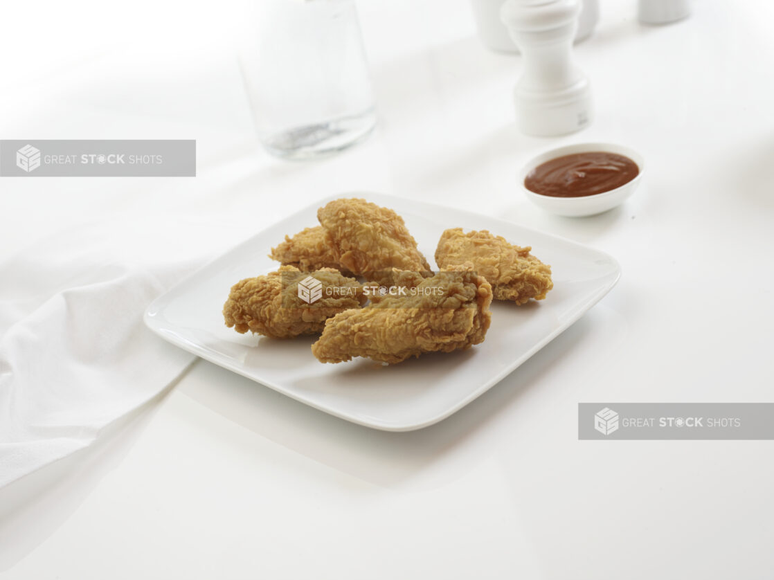 Plate of fried chicken wings on a white background with BBQ dipping sauce on the side