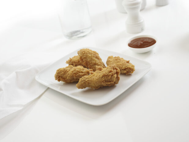 Plate of fried chicken wings on a white background with BBQ dipping sauce on the side