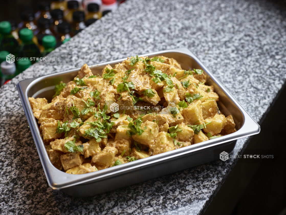 Metal tray of sauced middle eastern potatoes on a marble counter