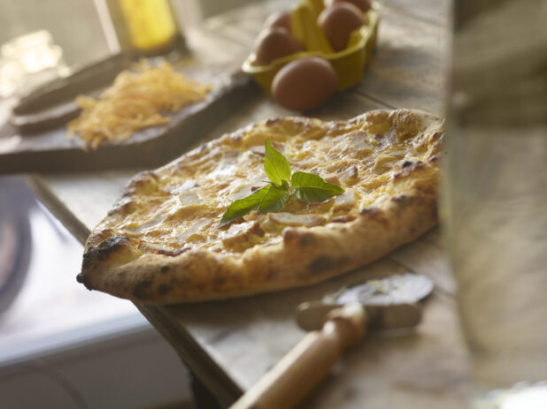 Whole chicken and cheddar cheese pizza on a wooden table with, items in background