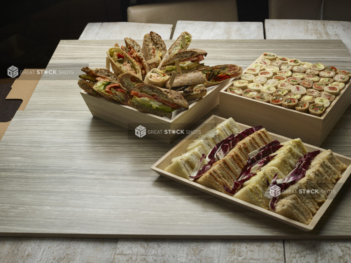 Various finger sandwiches on bread, bun and wraps on wooden trays on a wooden background