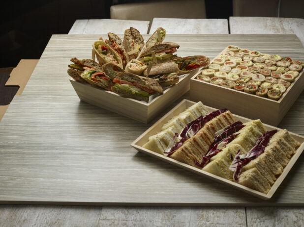 Various finger sandwiches on bread, bun and wraps on wooden trays on a wooden background