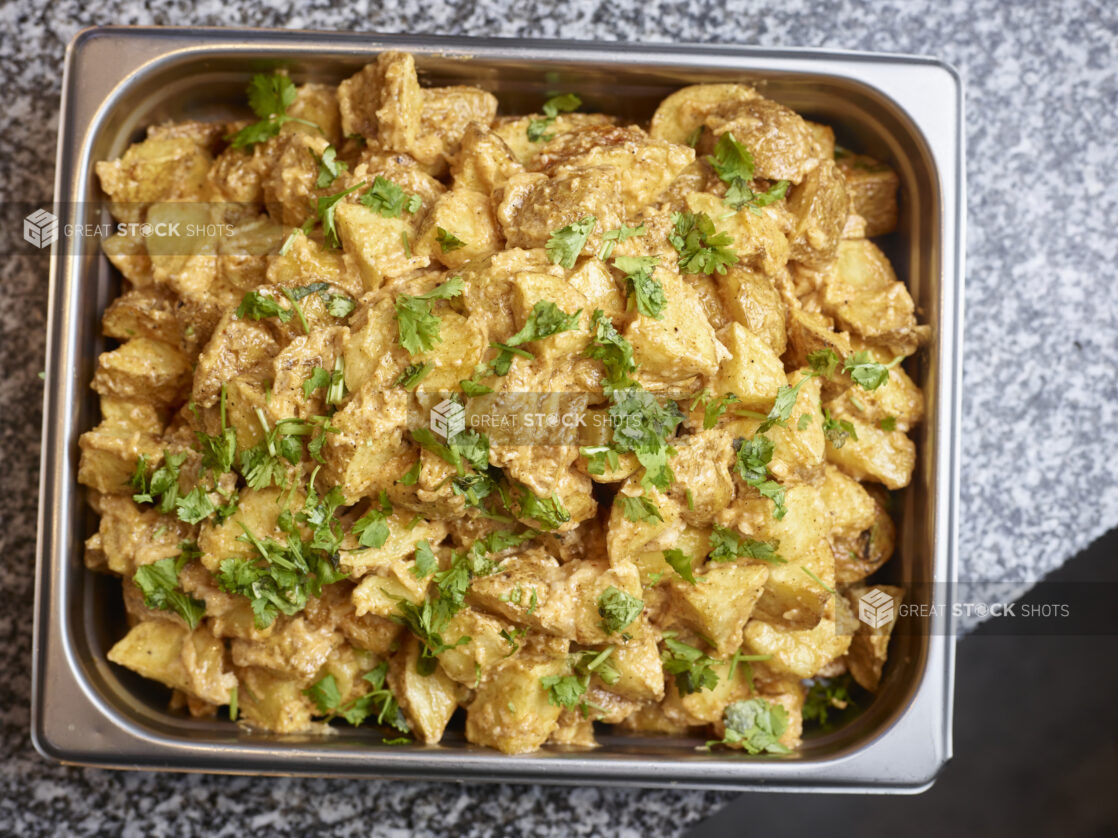 Above angle of sauced middle eastern potatoes in a metal tray on a marble counter