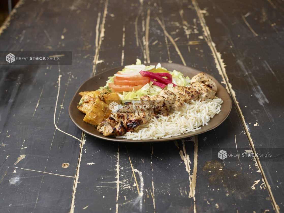 Middle eastern chicken souvlaki platter with rice, potatoes and salad on a distressed wooden background