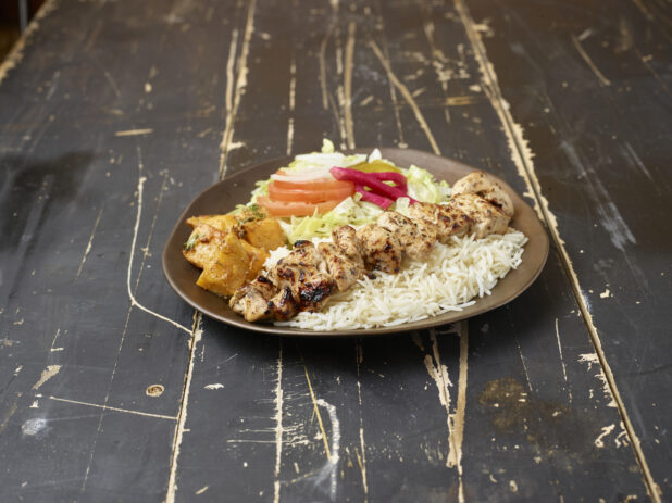 Middle eastern chicken souvlaki platter with rice, potatoes and salad on a distressed wooden background