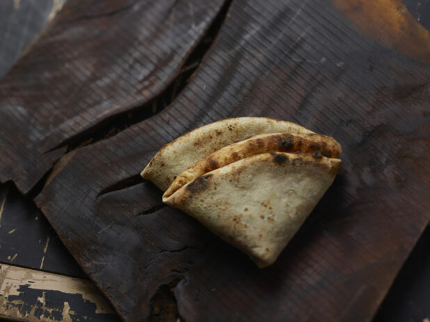 Folded wood fire pizza crust on a dark background, close-up