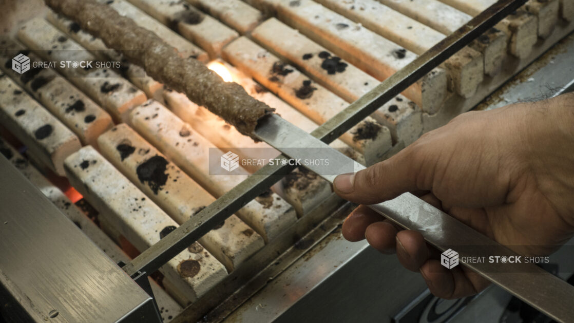 Man holding a skewers of kofta over an open charcoal flame