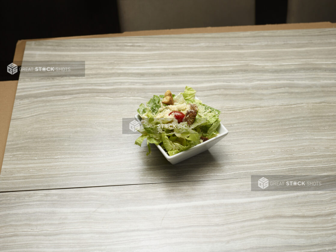 Overhead view of side caesar salad topped with parmesan and a cherry tomato on a wooden background