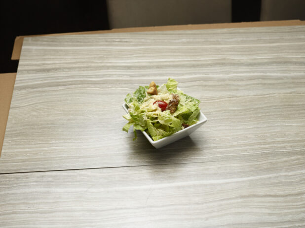 Overhead view of side caesar salad topped with parmesan and a cherry tomato on a wooden background