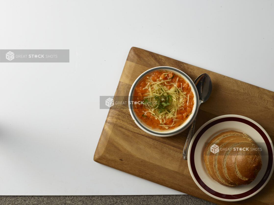 Bowl of chicken noddle soup with plate of rye bread in the background on a wooden board on a white background