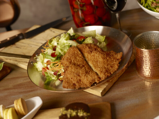 Crispy fried chicken with side garden salad on a metal frying pan