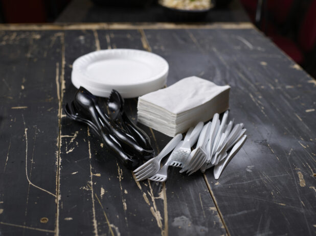 Collection of plastic cutlery and disposable plates and napkins on a distressed black wood background