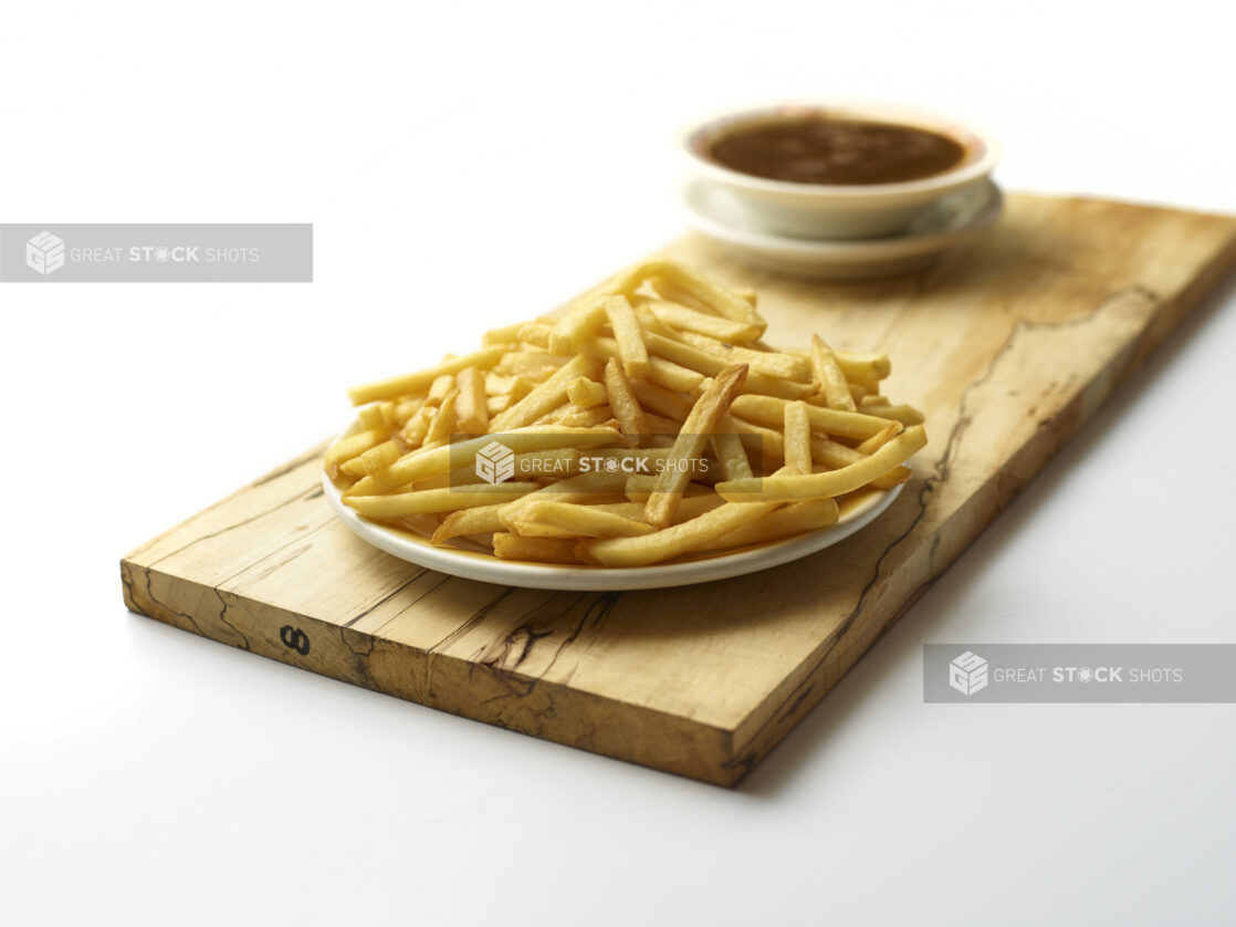 Plate of plain french fries with a bowl of soup in the background on a wooden board with a white background