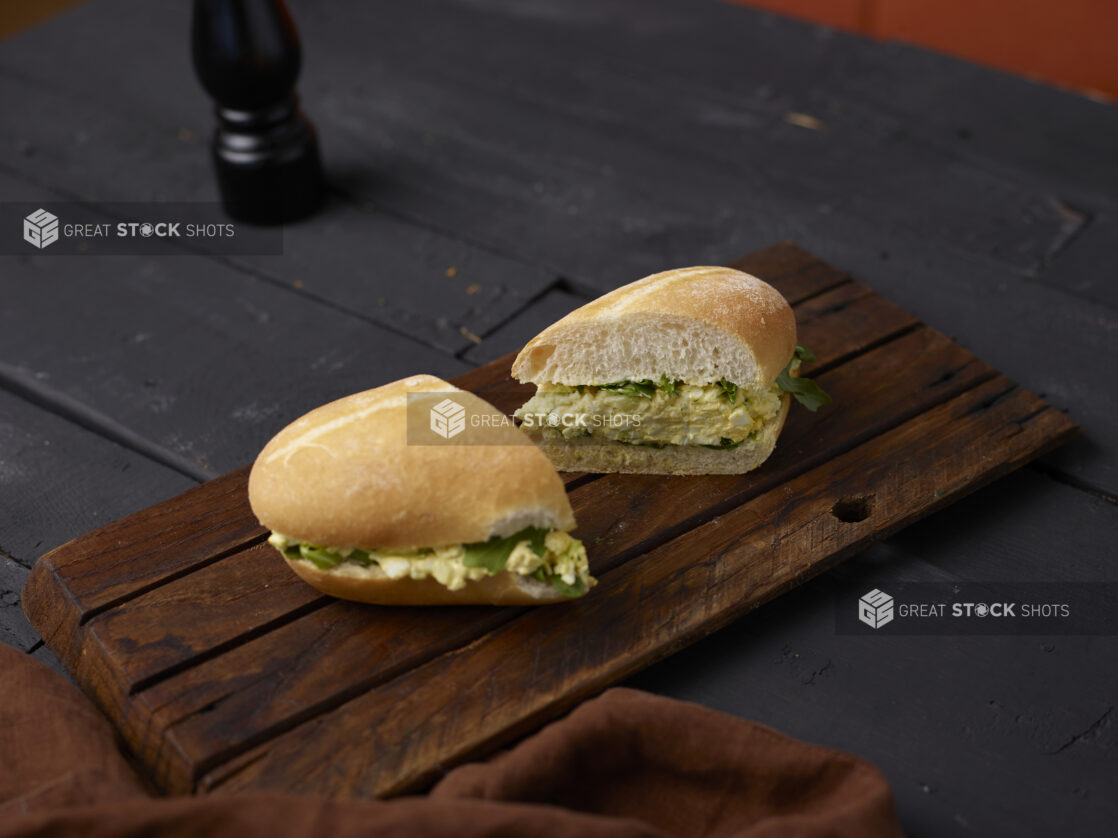 Egg salad sandwich on a white bun cut in half on a wooden board