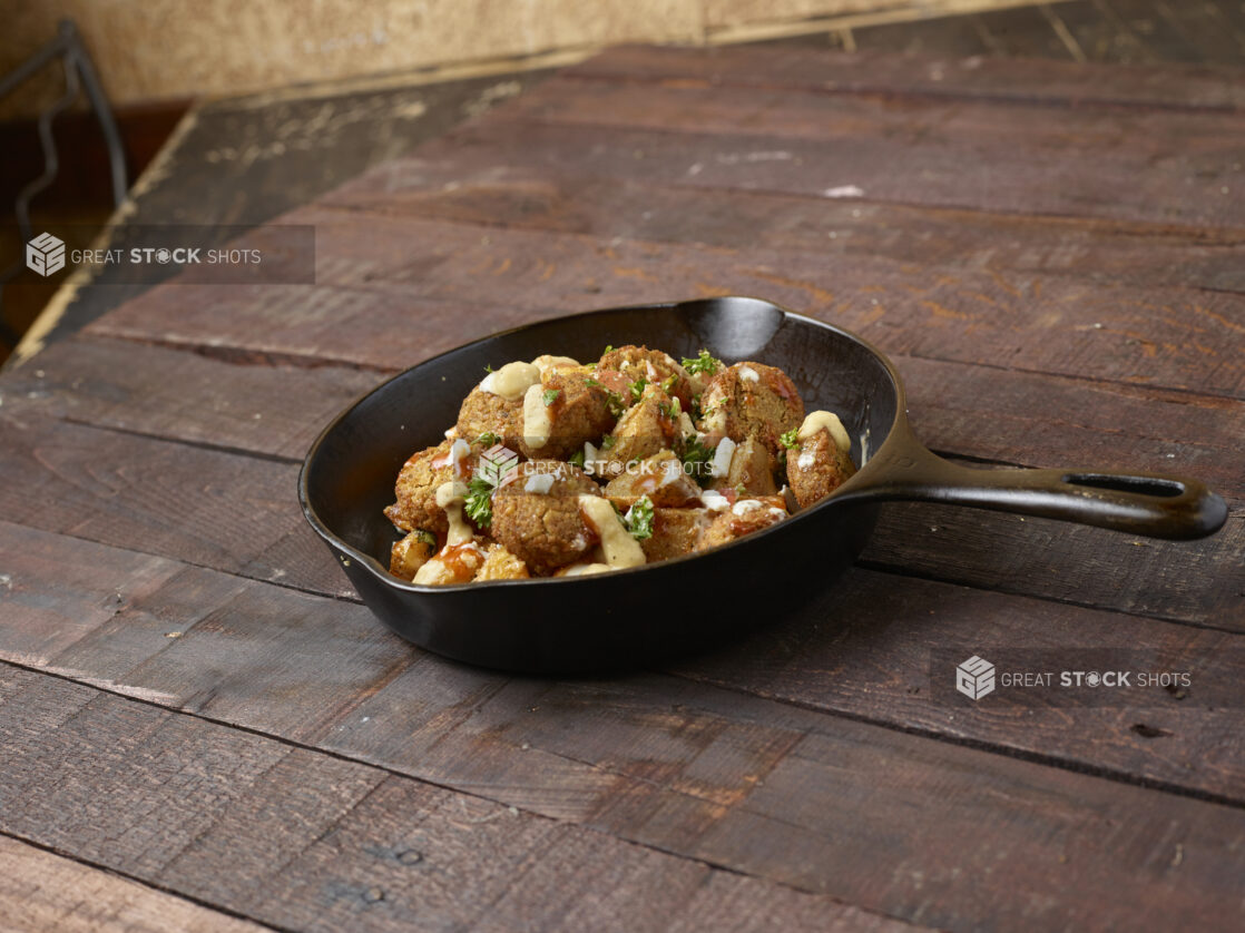 Falafel and potato skillet topped with tabouli on dark wood background