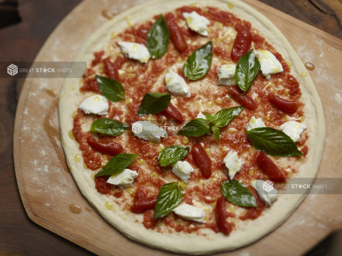 Whole uncooked margherita pizza on a wooden peel overhead