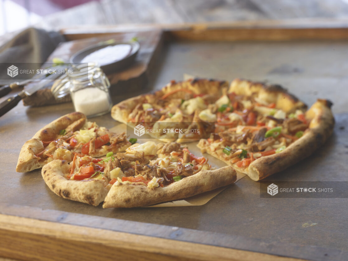 Sliced medium pulled pork pizza with red peppers and onion on parchment paper on a table